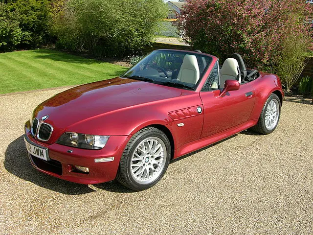 A black BMW Z3 parked on a patch of grass next to a road with the roof down