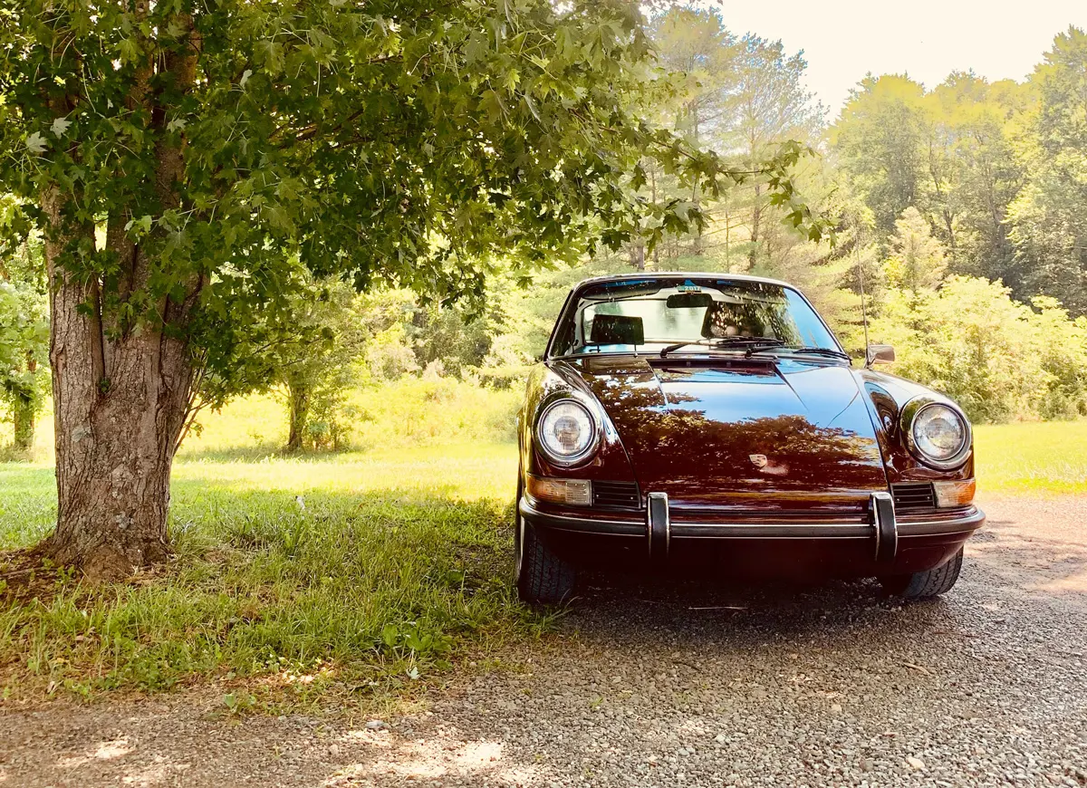 A classic Porsche parked under a tree on a sunny day