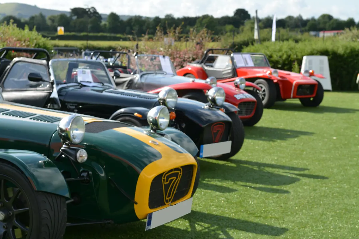Numerous models of Caterham cars lined up as a museum exhibit outside on green fake grass