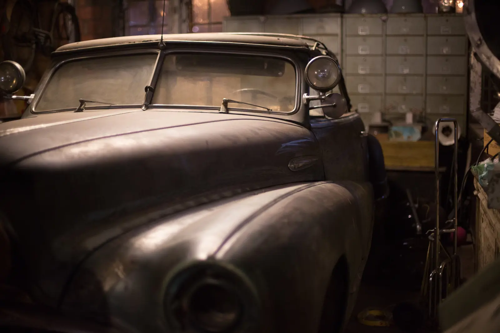 A dusty classic car parked in a garage during restoration