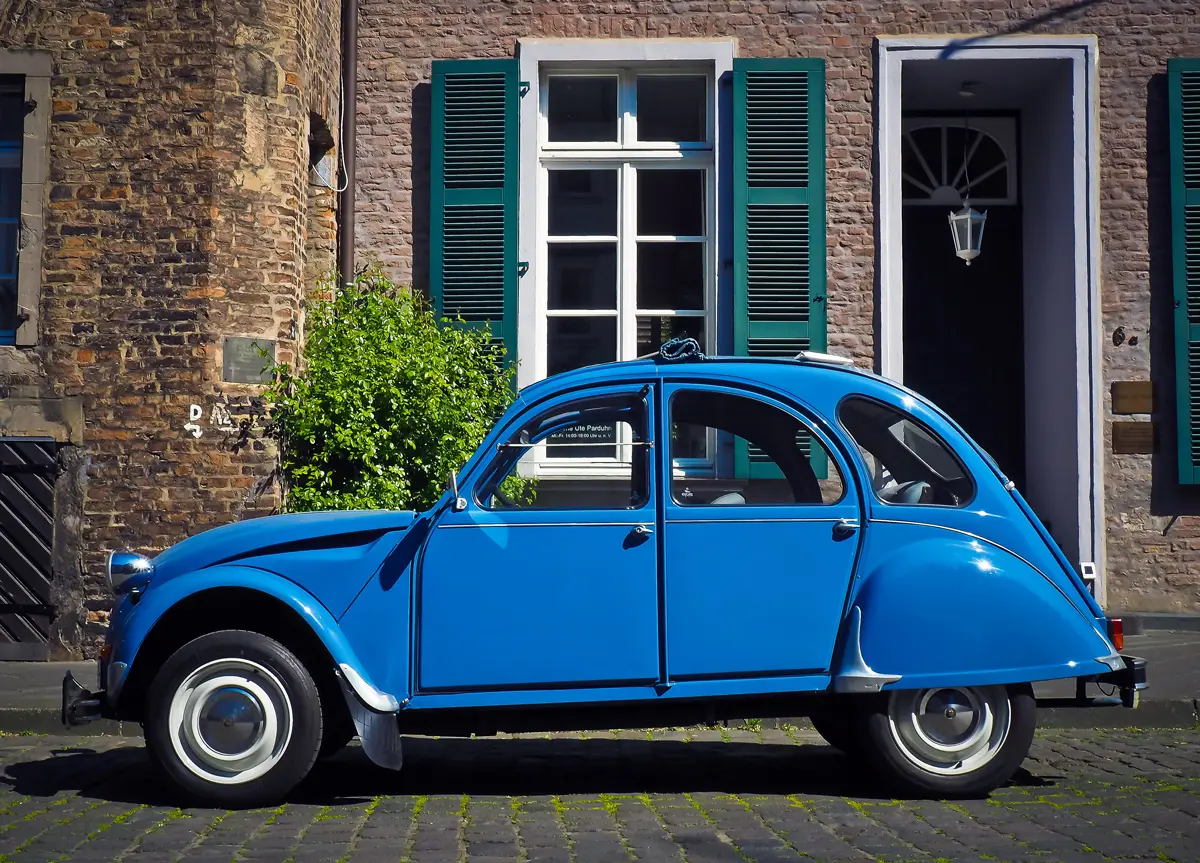 A blue Citroen 2CV parked outside a small pretty cottage on a sunny day