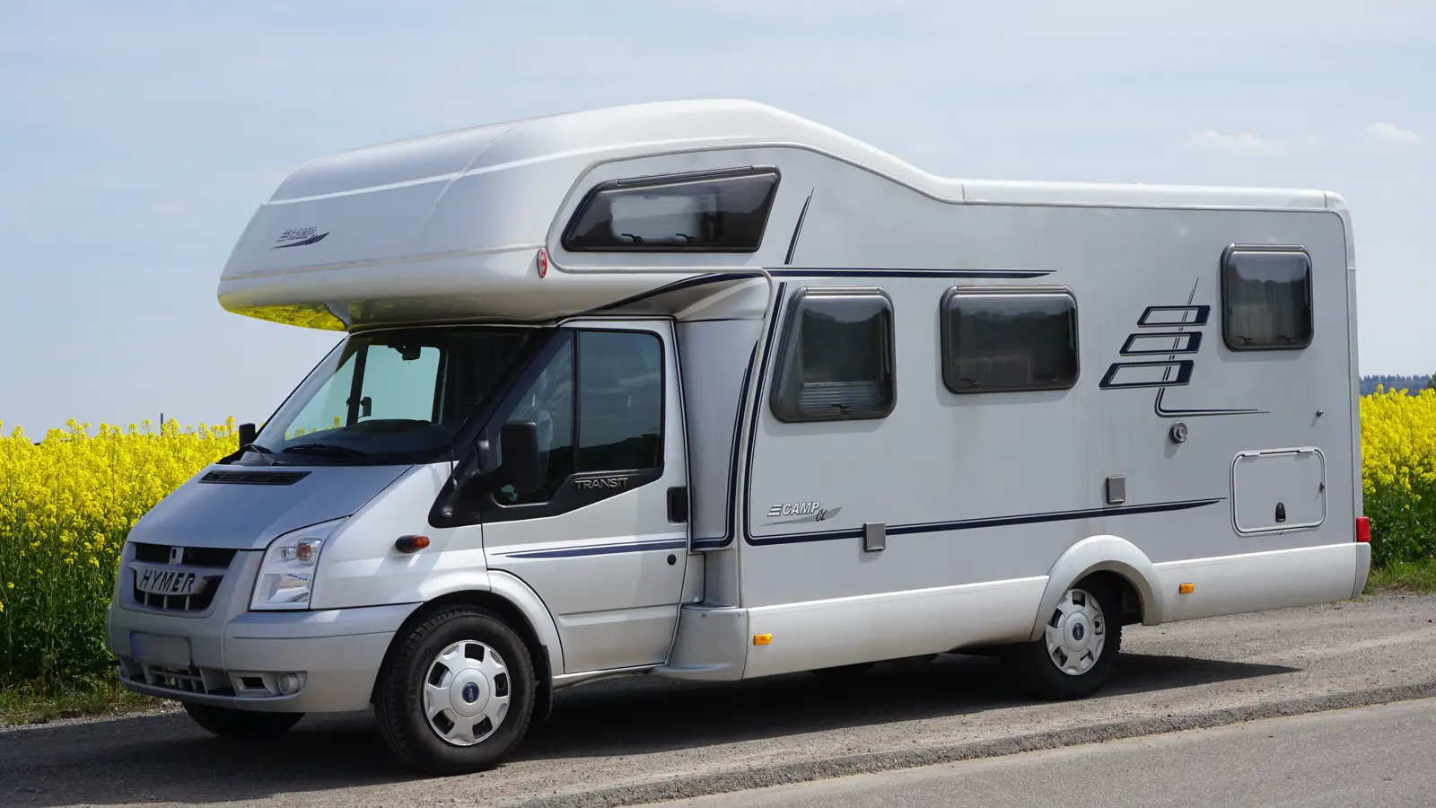 A motorhome parked at the side of the road in-front of a yellow crop field
