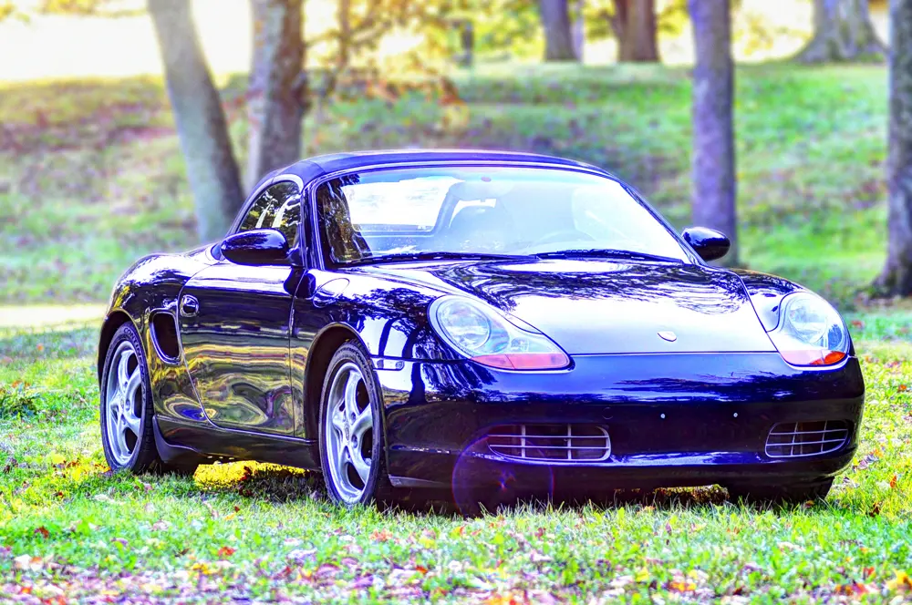 A classic Porsche Boxter parked on a grassy area with its roof up