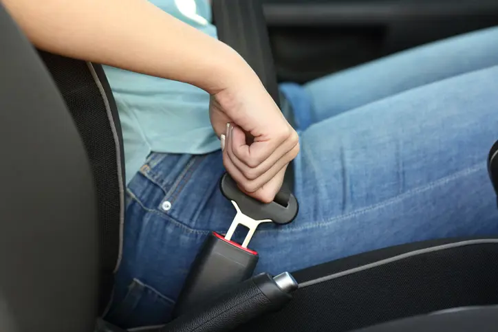 A person sitting in a car plugging their seatbelt in