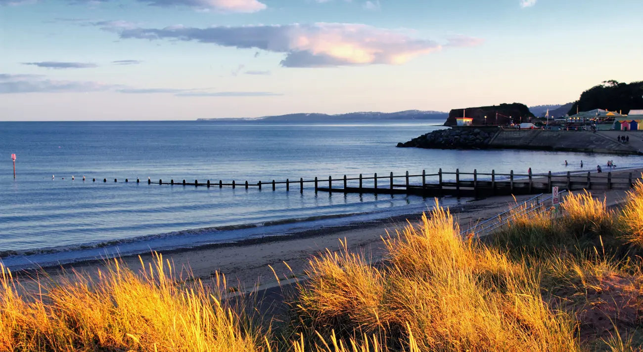 A sandy beach in Devon with a village behind at dusk