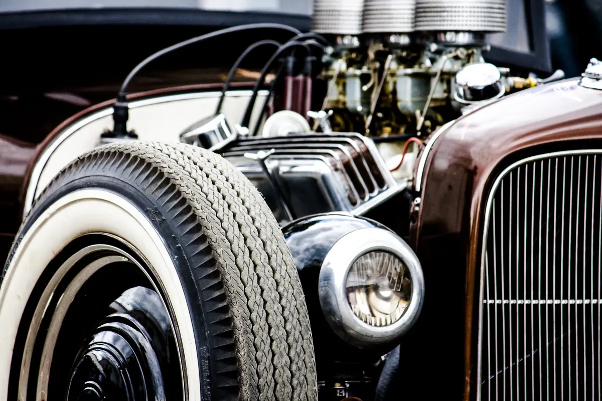 The front corner of a hot rod with its engine on display and white wall tyres