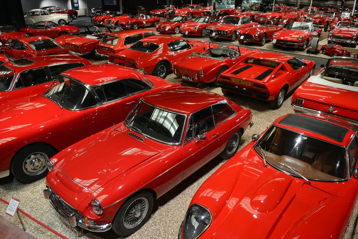 A large room in a museum filled with many red classic cars