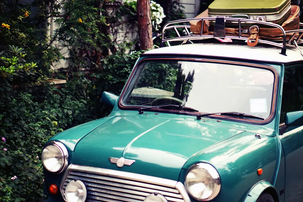 A teal classic mini with luggage loaded onto its roof rack