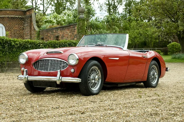 A convertible red Austin Healey parked on a gravel driveway
